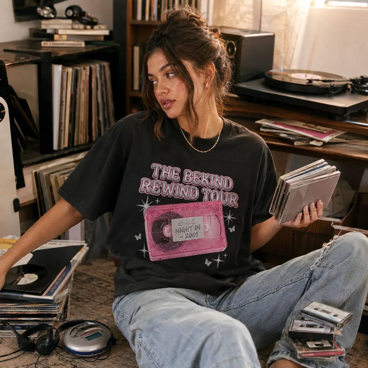 Girl holding CDs in a record-filled room while wearing a physical media graphic T-shirt - Outfit On Tour